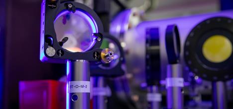 Close up of optics on a laser table. The lighting is deep purple and there is a pop of yellow on one of the optics.