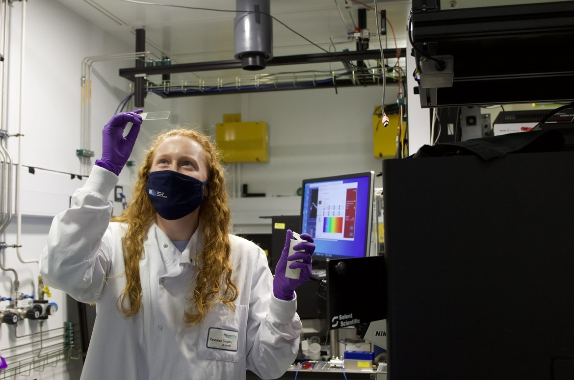 Ellen in one of the Octopus microscopy labs, in a lab coat and gloves, examining a microscope slide