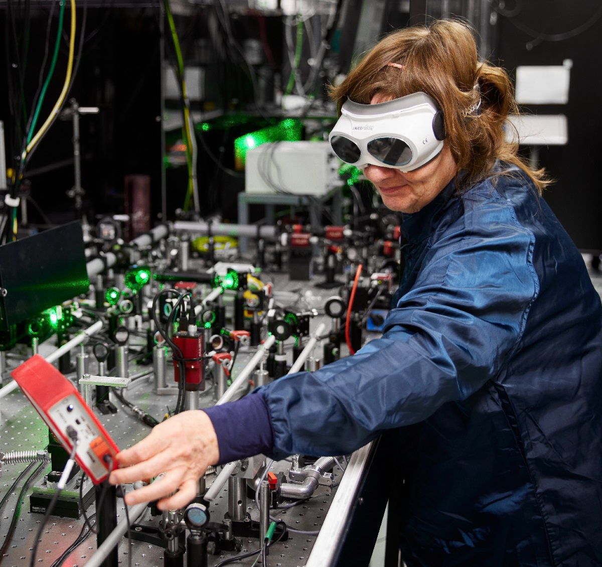 Victoria wearing a lab coat and laser goggles adjusting electronics in a Gemini lab.​