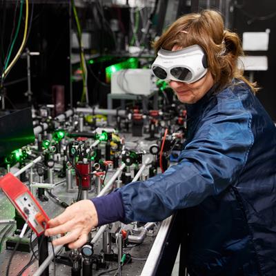 Victoria wearing a lab coat and laser goggles while adjusting optics in a Gemini lab.