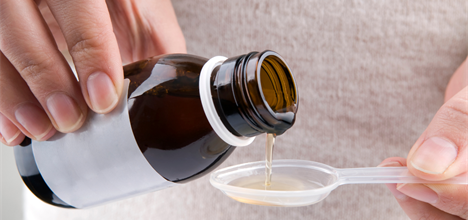 Close-up liquid medicine being poured into a teaspoon