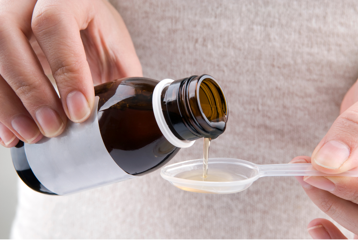 Close-up liquid medicine being poured into a teaspoon