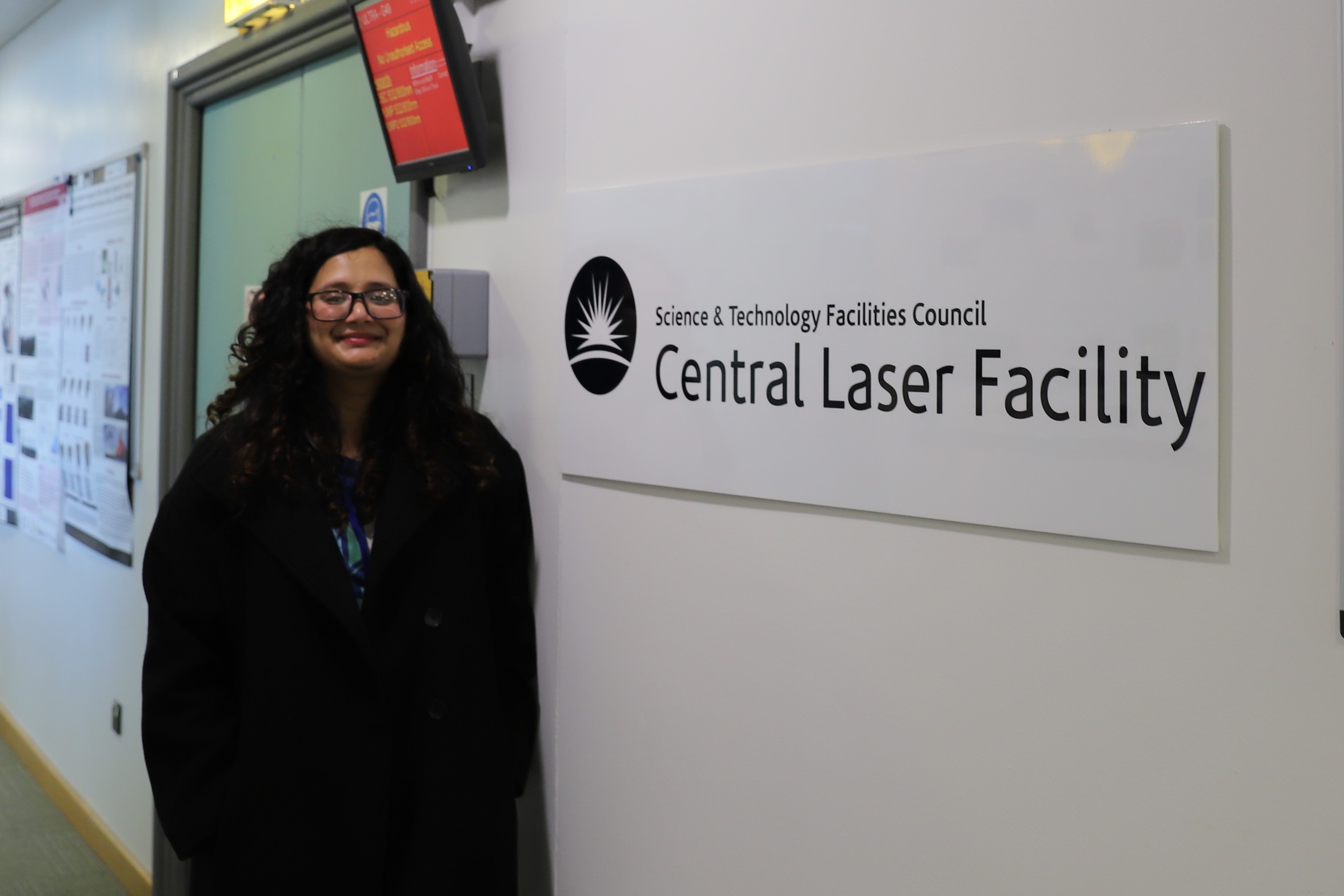 Sneha standing next to a sign that reads "Science and Technology Facilities Council Central Laser Facility".