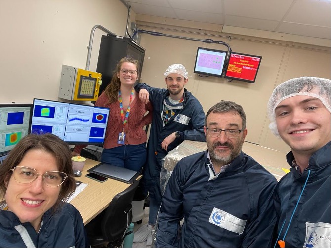 Photo of 5 smiling people next to some screens showing data from the laser. 