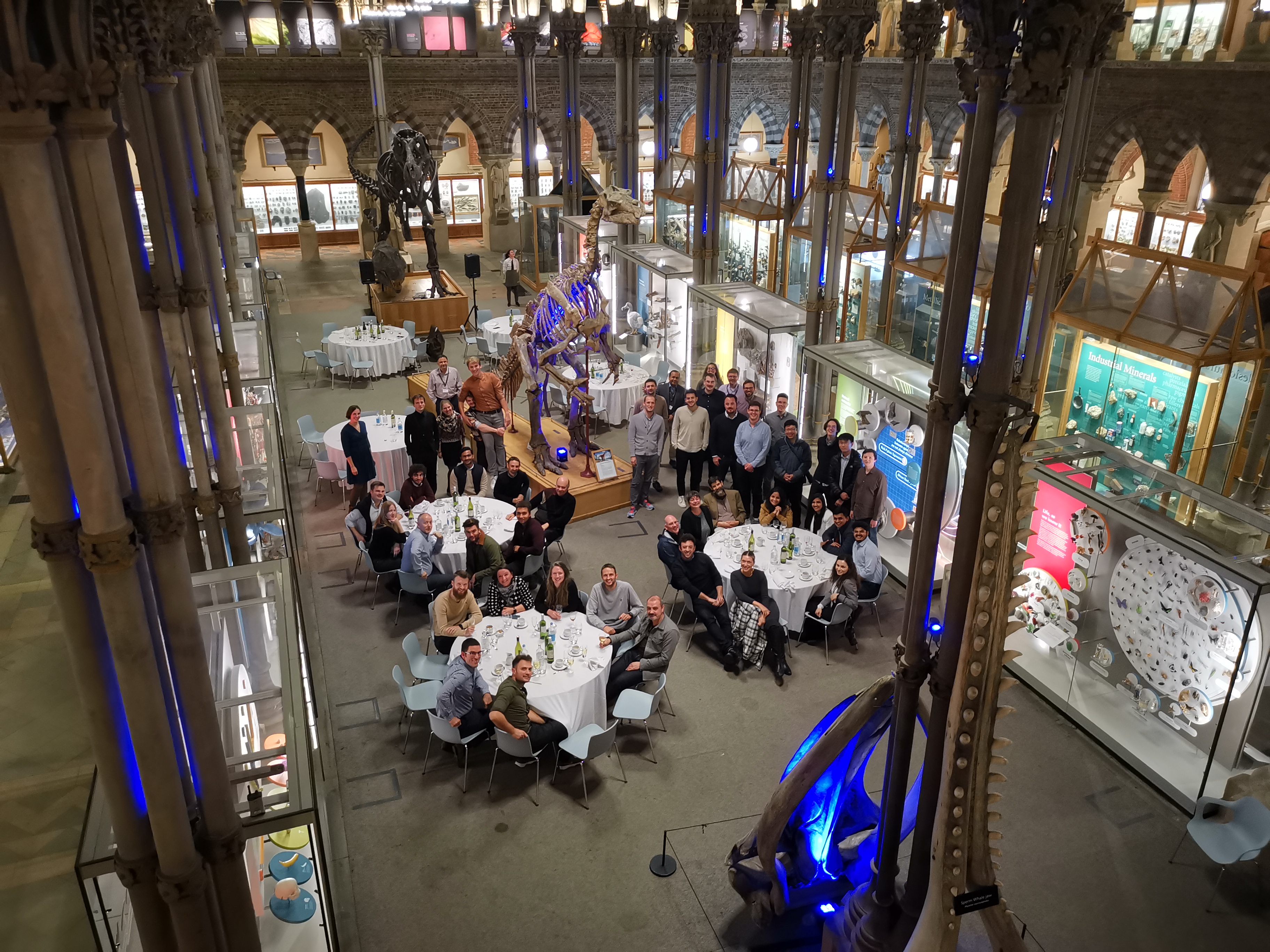 People sitting around tables amongst dinosaur skeletons in Oxford Natural History Museum