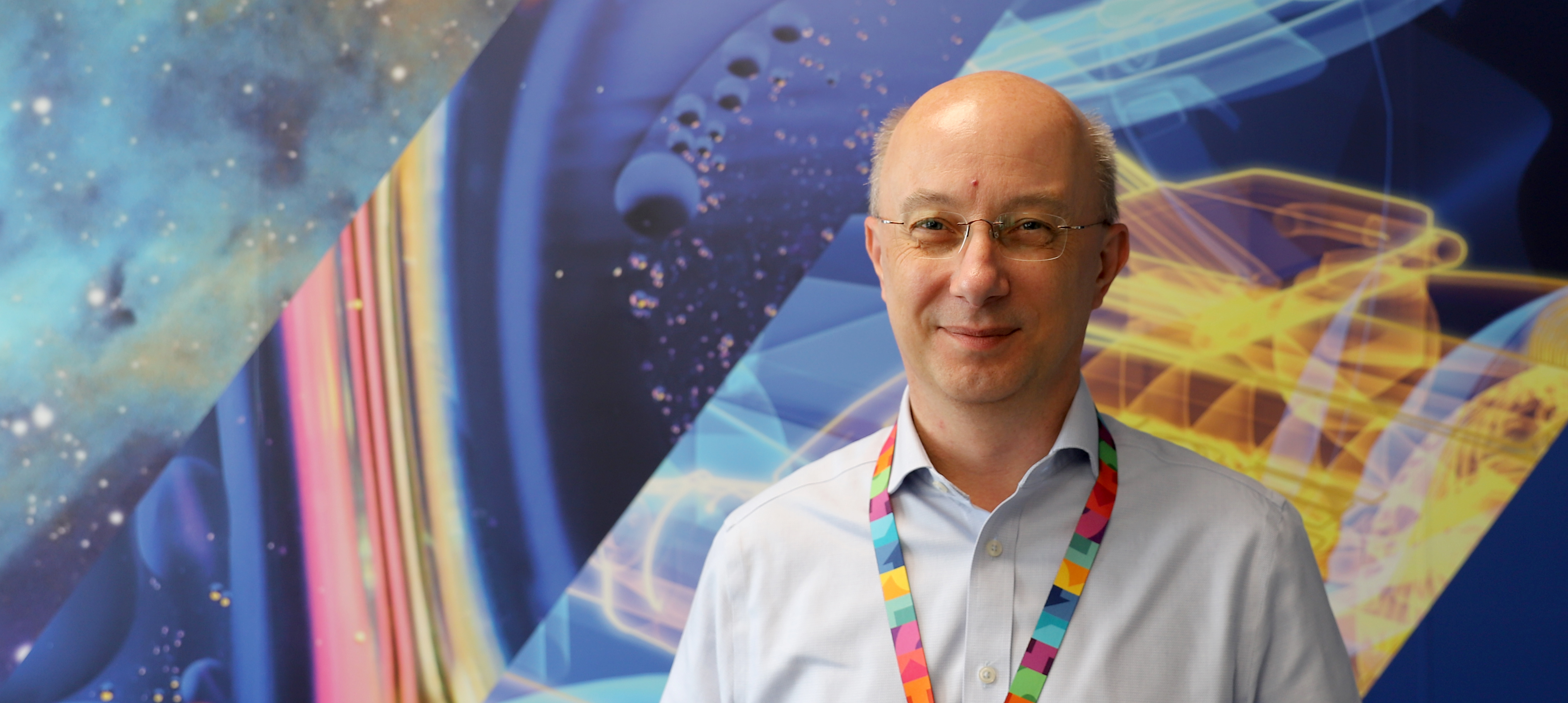 Prof David Newbold stands infront of a blue wall mural.